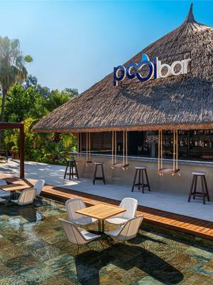 Thatched-roof Pool Bar at Rixos Göcek surrounded by lush greenery, featuring in-water seating, wooden decks, and hanging swing stools under a tropical-style canopy.
